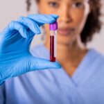 A physician holds up a vial of blood, signifying the difference between genetic testing and cancer blood test.